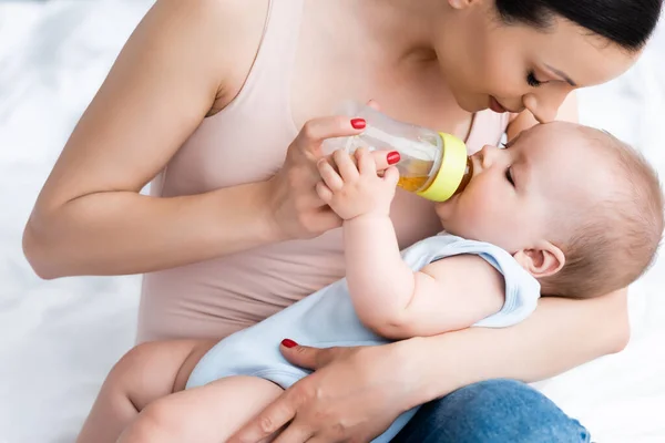 Mutter füttert niedlichen Säugling Sohn, während sie Babyflasche hält — Stockfoto