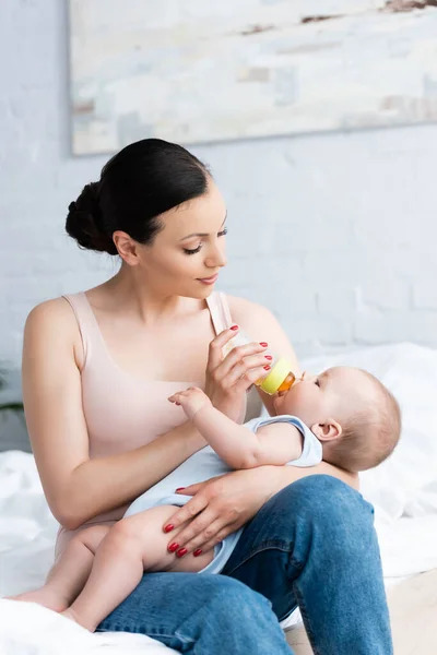 Красива жінка годує милого хлопчика, тримаючи пляшку для немовлят — стокове фото