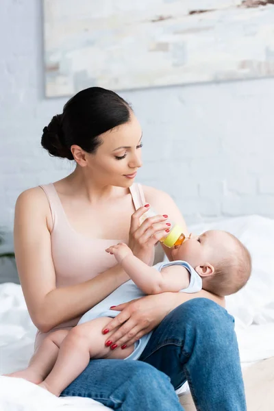 Beautiful woman feeding cute baby boy while holding baby bottle — Stock Photo