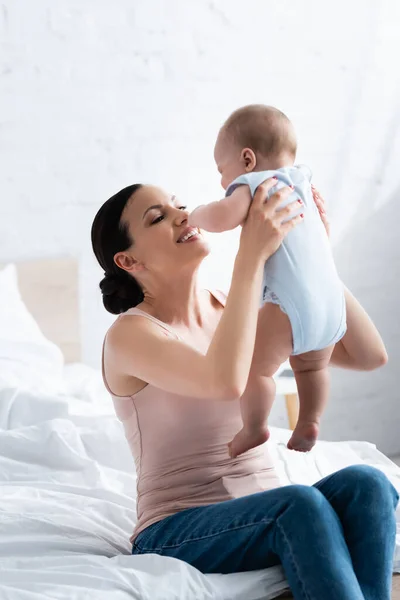 Alegre madre sosteniendo en brazos lindo bebé hijo con los pies desnudos - foto de stock