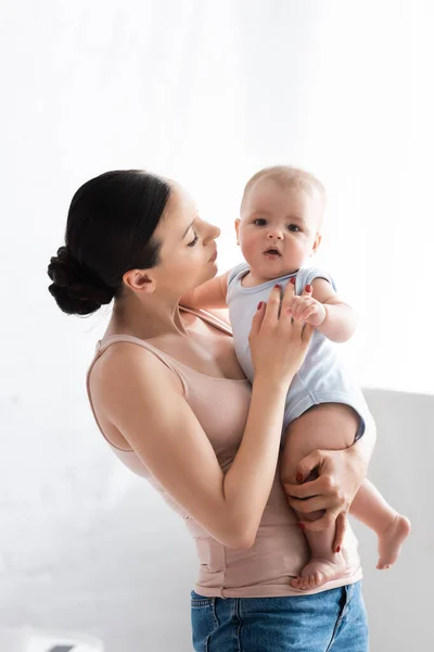 Madre sosteniendo en brazos lindo bebé hijo con los pies desnudos - foto de stock