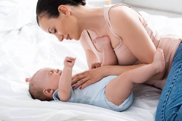 Atractiva madre mirando llorando bebé niño en el dormitorio - foto de stock