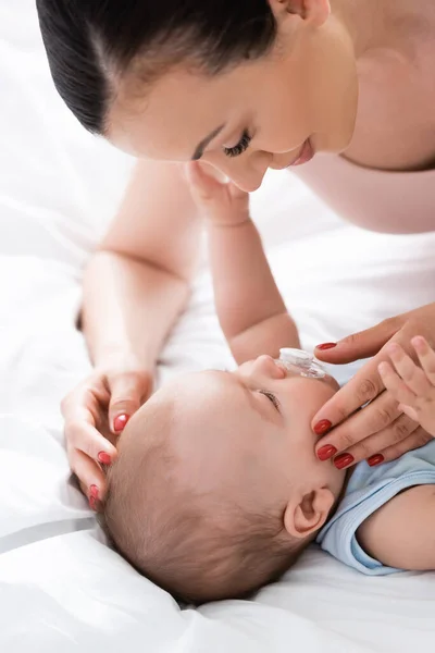 Attractive mother looking at infant son with baby binky — Stock Photo