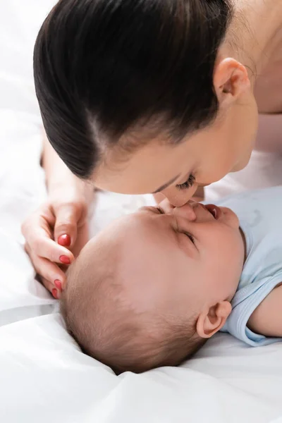 Atractiva madre e hijo pequeño tocando narices en el dormitorio - foto de stock