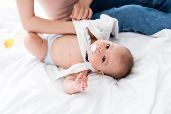 Mãe sentada na cama enquanto vestindo bebê romper no filho bebê — Fotografia de Stock