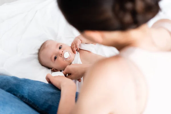 Selective focus of cute infant boy with pacifier looking at mother — Stock Photo