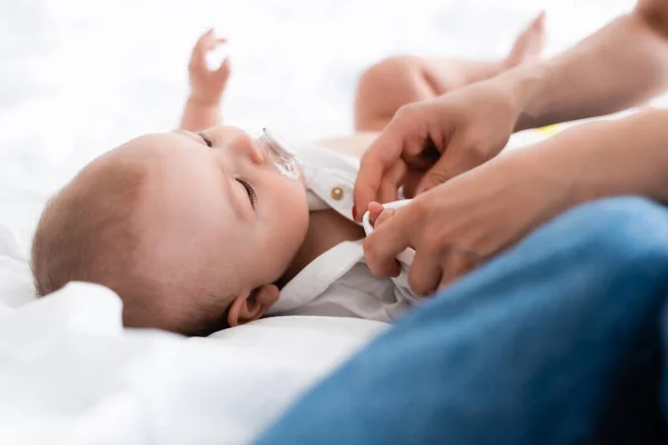 Foco seletivo da mãe vestindo bebê romper no filho bebê bonito com chupeta — Fotografia de Stock