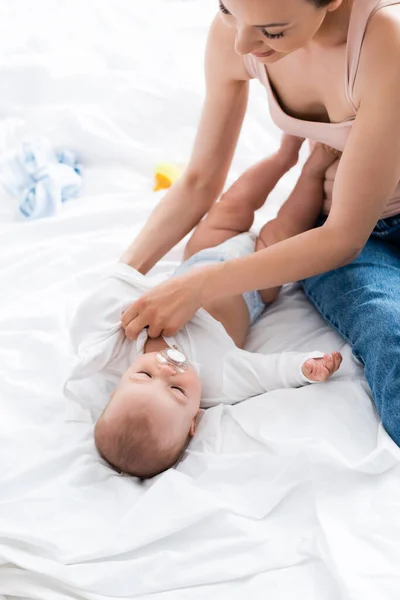 Happy mother wearing baby romper on cute infant son with pacifier — Stock Photo