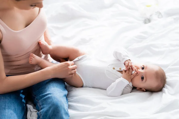 Messa a fuoco selettiva della madre che indossa pagliaccetto bambino sul bambino con ciuccio guardando la fotocamera — Foto stock