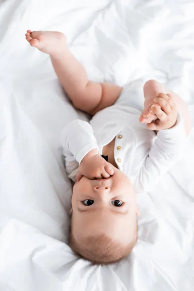 Vue de dessus de bébé garçon sucer la main tout en étant couché sur le lit — Photo de stock