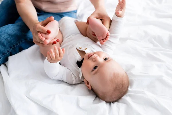 Mother touching bare feet of cute infant son in baby romper — Stock Photo