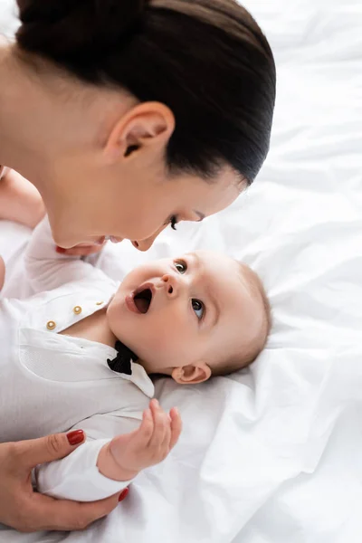 Mother looking at cute infant son with open mouth in bedroom — Stock Photo