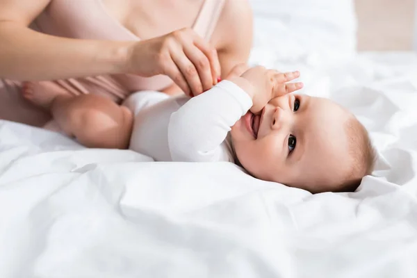 Selective focus of mother touching happy infant son in baby romper on bed — Stock Photo