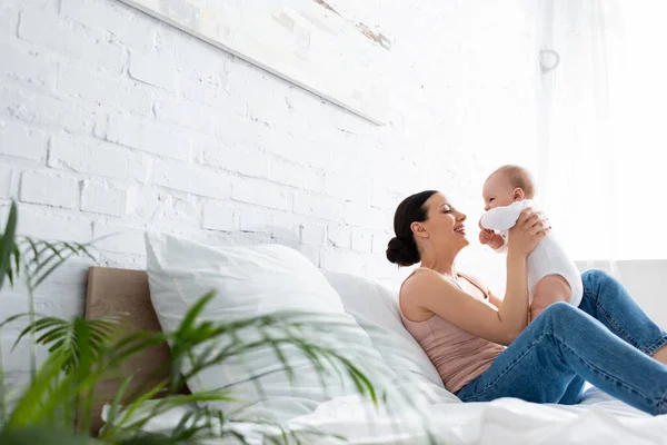 Selektiver Fokus der glücklichen Mutter, die auf dem Bett sitzt und ihren niedlichen Säugling im Arm hält — Stockfoto