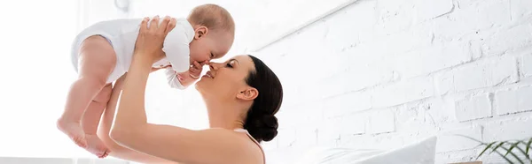 Панорамная концепция счастливой матери, держащей в руках милого младенца сына в спальне — стоковое фото