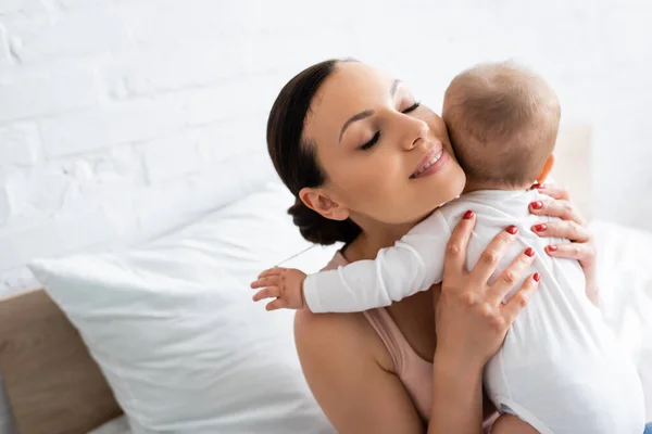 Vista aérea de la mujer feliz con los ojos cerrados abrazando adorable bebé niño - foto de stock