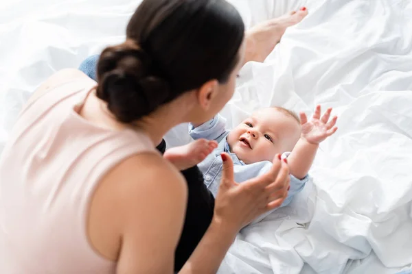 Vista aérea de la madre en vaqueros sentados en la cama cerca de lindo hijo pequeño - foto de stock