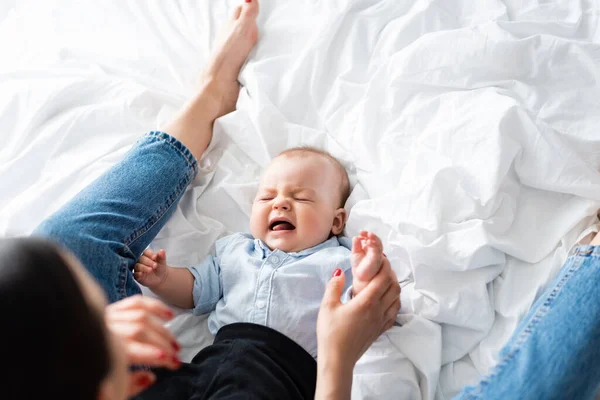 Vue du dessus de l'enfant garçon pleurant sur le lit près de la mère — Photo de stock