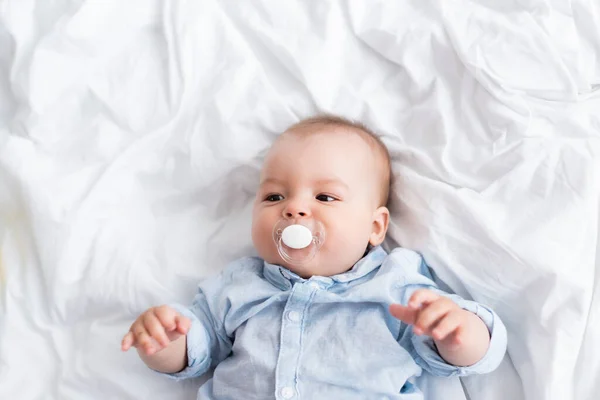 Top view of infant boy with pacifier lying on bed — Stock Photo