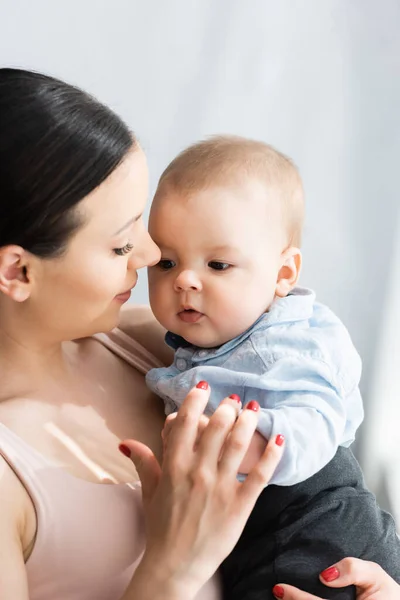 Bela mãe segurando nos braços bonito bebê filho em roupas de bebê — Fotografia de Stock