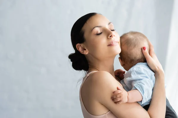 Щаслива мати з закритими очима тримає в руках милий немовля сина в дитячому одязі — Stock Photo