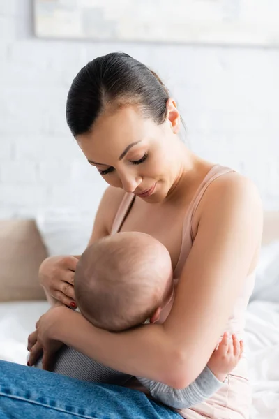 Mother looking at infant boy while breastfeeding in bedroom — Stock Photo