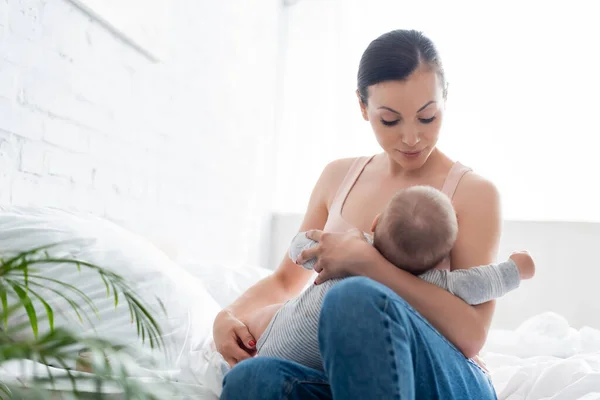 Selective focus of attractive mother looking at infant son while breastfeeding in bedroom — Stock Photo