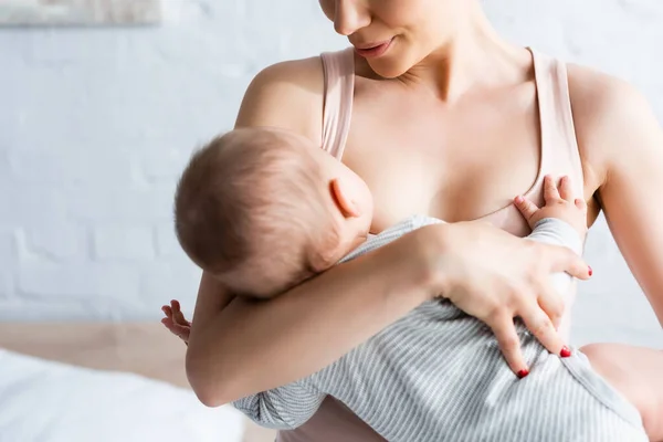 Обрізаний вид матері грудного вигодовування дитини хлопчика в спальні — стокове фото