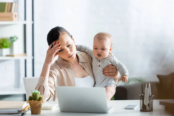 Selective focus of upset mother looking at laptop and holding infant son — Stock Photo