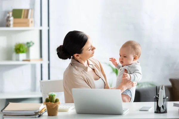 Избирательный фокус матери, глядя на младенца сына рядом с цифровыми устройствами — стоковое фото