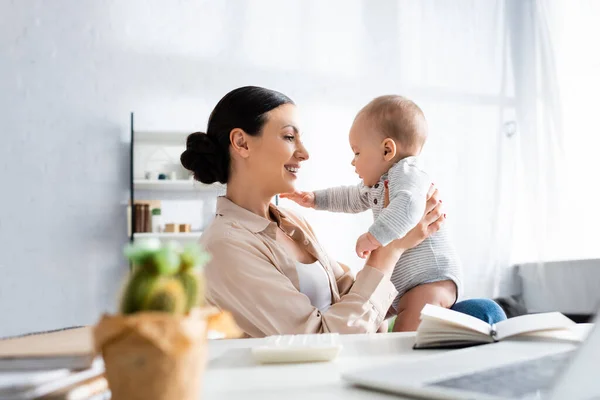 Selective focus of happy mother looking at infant son near notebook — Stock Photo