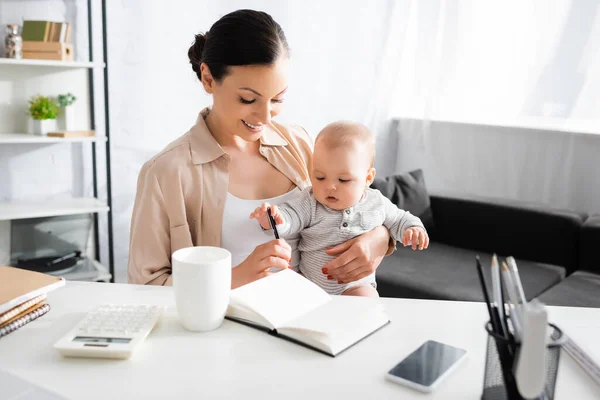 Селективное внимание счастливой матери, держащей ручку рядом с младенцем — стоковое фото