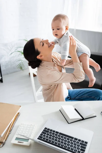Selective focus of happy mother holding in arms cute infant son near laptop — Stock Photo