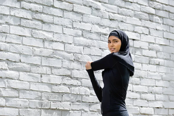 Chica musulmana atractiva en hijab ejercicio cerca de la pared de ladrillo - foto de stock