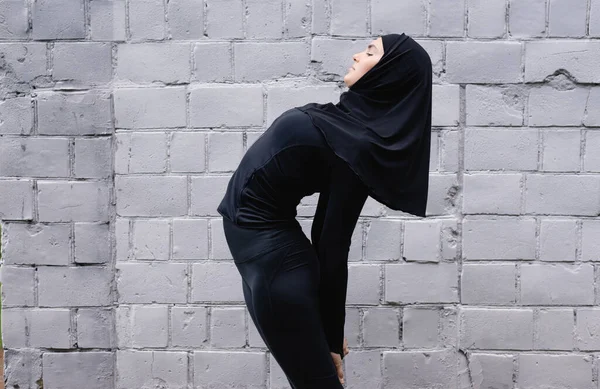 Профиль мусульманской спортсменки, растянувшейся у кирпичной стены — стоковое фото