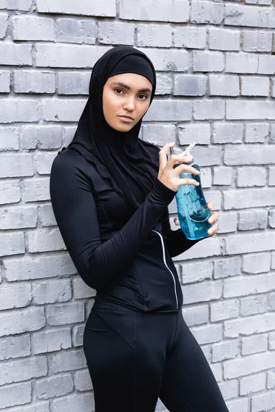 Joven deportista musulmana en hijab sosteniendo botella deportiva con agua - foto de stock