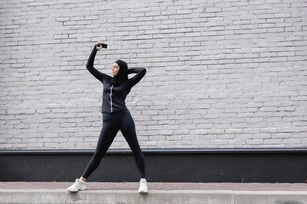 Muslimische Frau hält Smartphone mit leerem Bildschirm nahe Ziegelmauer — Stockfoto