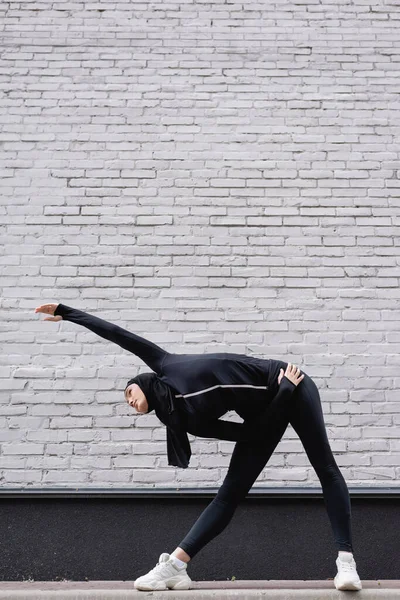 Arabian sportswoman in hijab exercising near brick wall — Stock Photo