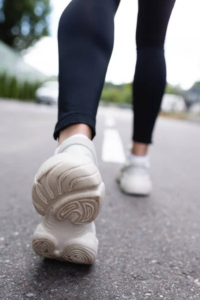 Foco selectivo de zapatillas blancas de mujer deportista haciendo ejercicio sobre asfalto - foto de stock