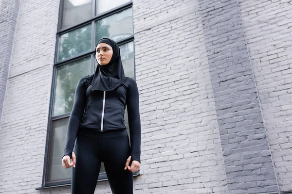 Vue à angle bas de la jeune femme musulmane en hijab debout près du bâtiment — Photo de stock