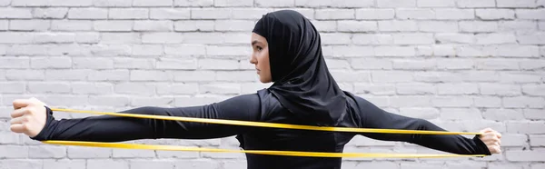 Horizontal image of arabian sportswoman in hijab exercising with resistance band — Stock Photo