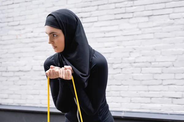 Árabe menina no hijab exercício com resistência banda perto de tijolo parede — Fotografia de Stock