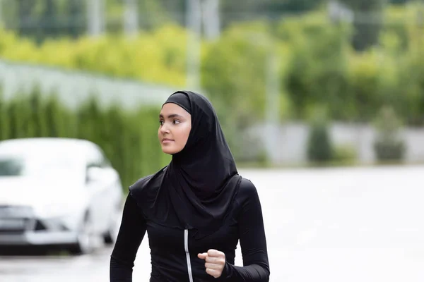 Arabian sportswoman in hijab and sportswear jogging and looking away — Stock Photo