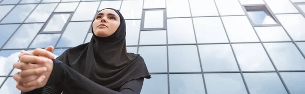 Горизонтальна концепція мусульманської жінки в хіджабі, що стоїть біля сучасної будівлі — стокове фото