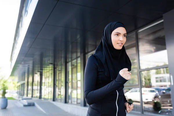 Young muslim sportswoman in hijab running near building — Stock Photo