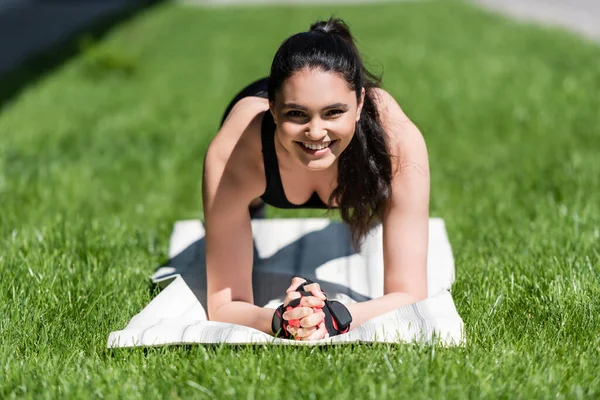 Enfoque selectivo de la deportista feliz haciendo tablón en la alfombra de fitness fuera - foto de stock