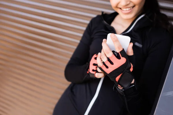 Cropped view of happy girl holding smartphone and smiling outside — Stock Photo