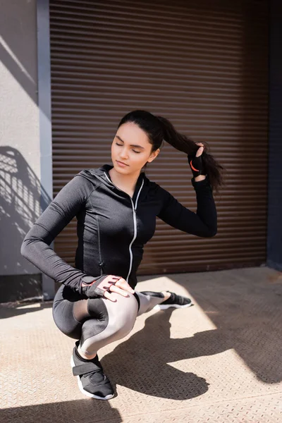 Selektiver Fokus der schönen jungen Sportlerin, die sich draußen dehnt, während sie Haare berührt — Stockfoto