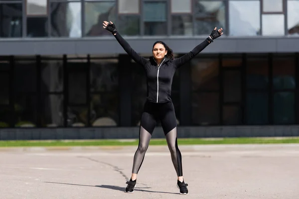 Attractive young sportswoman with outstretched hands working out on asphalt — Stock Photo