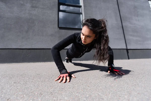 Junge Sportlerin beim Planken auf Asphalt nahe Betonmauer — Stockfoto